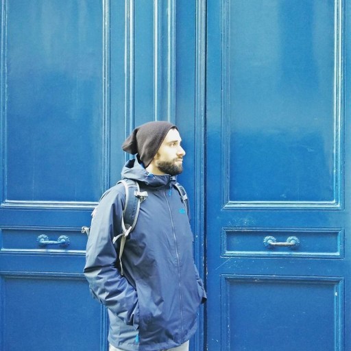Radimir with a black, short beard, a black heat, a blue jacket in front of a blue door. 